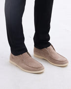 Beige suede shoes worn with black pants on a white background