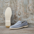 Light blue loafers with white soles against a textured wall.