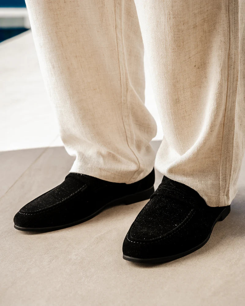 Man wearing suede penny loafers with tailored cream-colored trousers.
