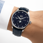 Luxury watch with dark blue face and black strap worn on a wrist against a white background