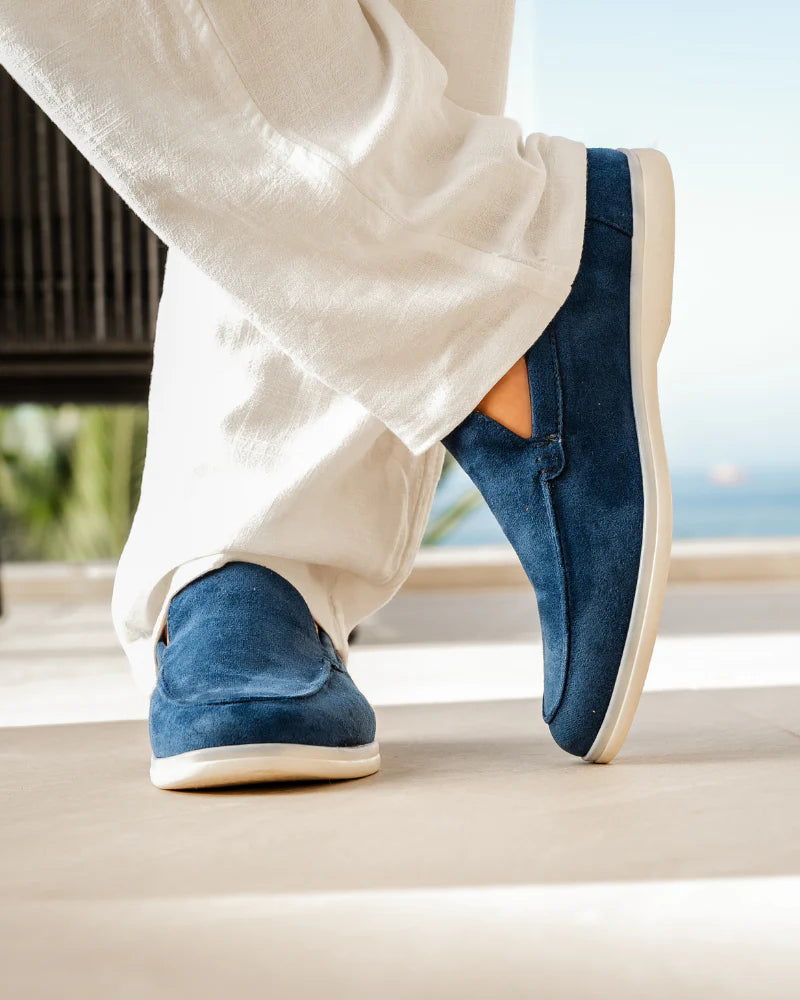 Blue loafers worn with white pants on a neutral background