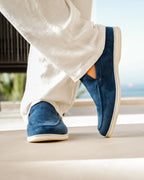 Blue loafers worn with white pants on a neutral background