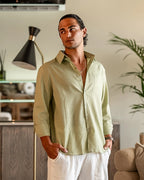 Man wearing a light green shirt and white pants in a modern living room.