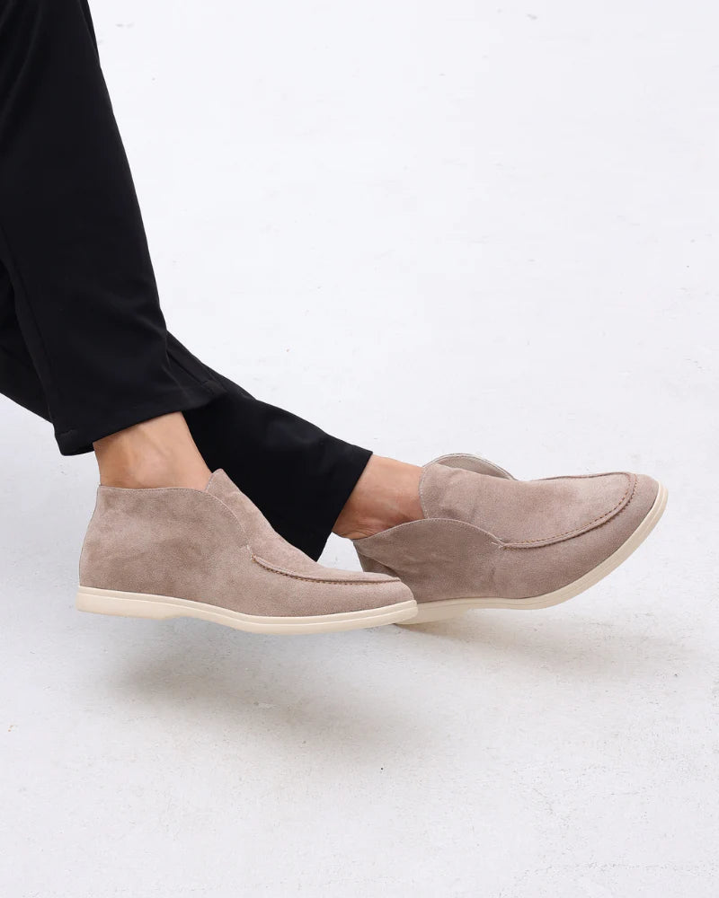 Beige slip-on shoes worn with black pants on a light gray background