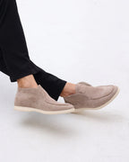 Beige slip-on shoes worn with black pants on a light gray background