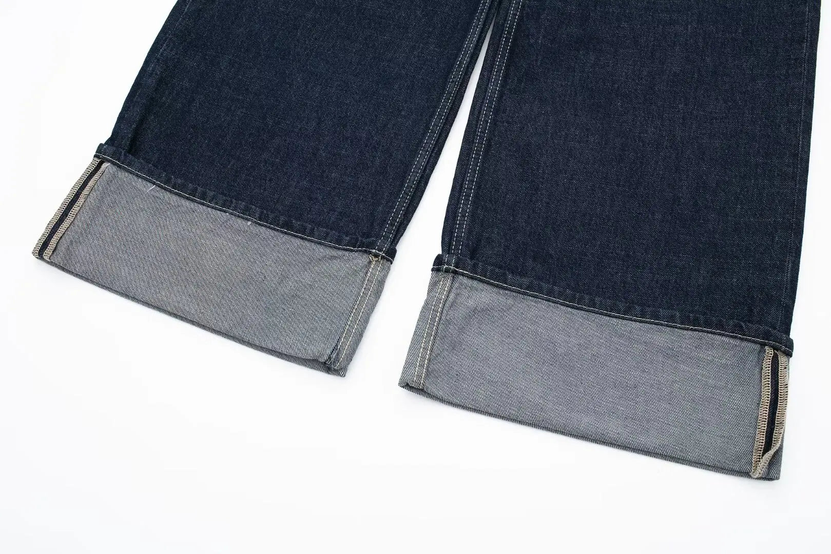 Close-up of dark blue jeans with gray cuffs on a white background