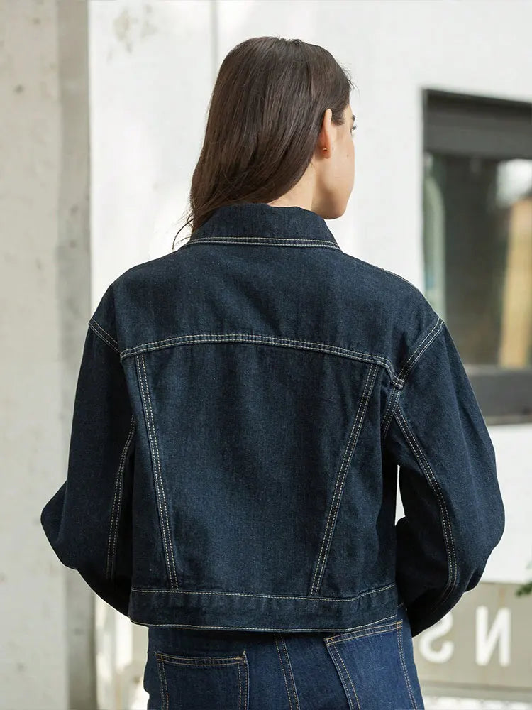 Person wearing a dark blue denim jacket standing against a light-colored wall.