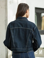 Person wearing a dark blue denim jacket standing against a light-colored wall.