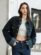 Woman wearing a denim jacket and jeans standing against a light-colored wall.