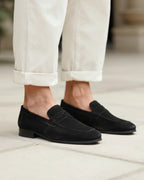 Black loafers worn with light-colored pants on a neutral background