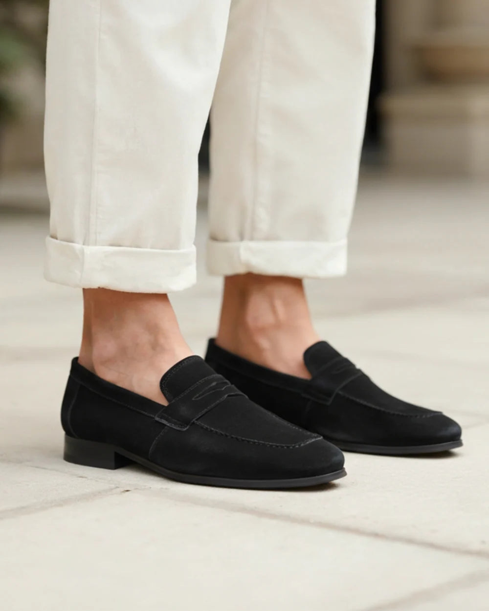 Black loafers worn with light-colored pants on a neutral background