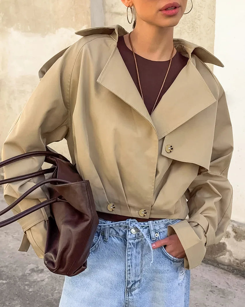 Person wearing a beige trench coat with a brown bag and light blue jeans.