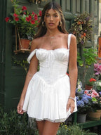 Woman in a white dress standing in front of a garden with flowers and plants.