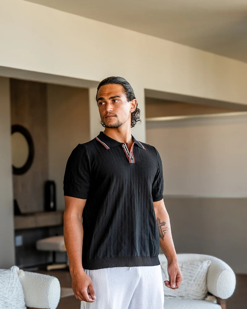 Man wearing a black polo shirt with red and white accents in a living room setting