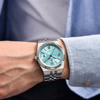 Close-up of a wrist wearing a silver watch with a turquoise face, against a blurred background.