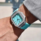 Turquoise watch with silver case on a wrist against a blurred outdoor background