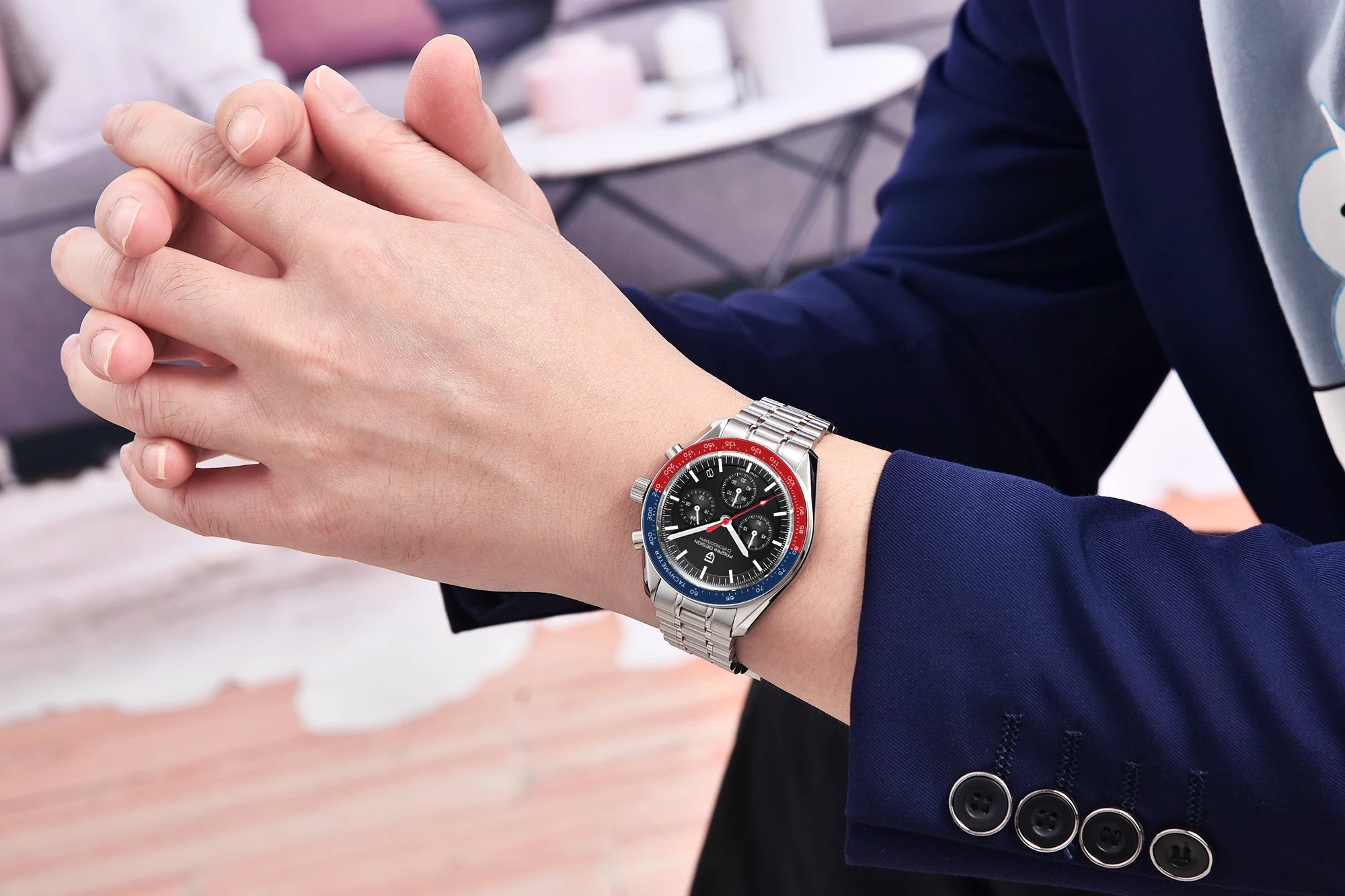 Person wearing a silver watch with red and blue accents on a blurred indoor background