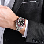 Person wearing a silver watch with a black and red face on a suit sleeve.