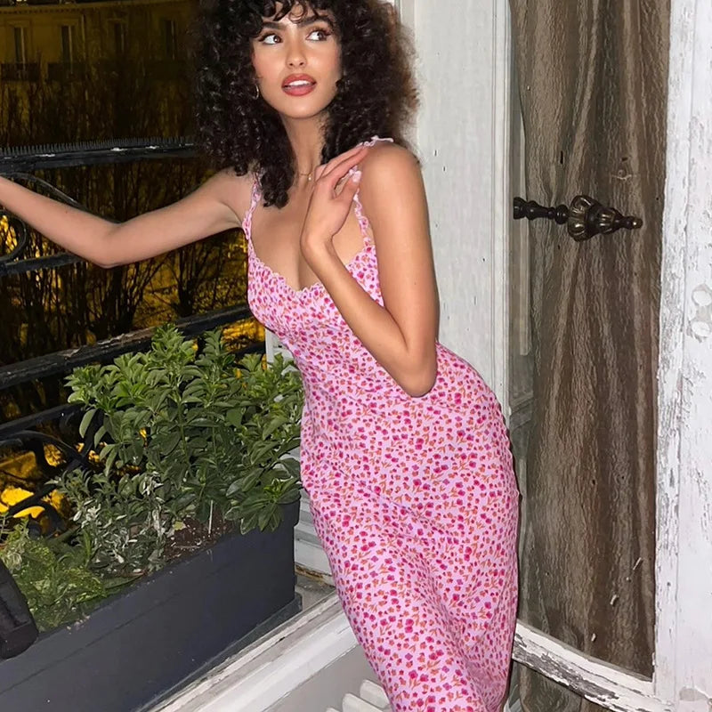 Woman in a pink floral dress standing by a door with plants in the foreground