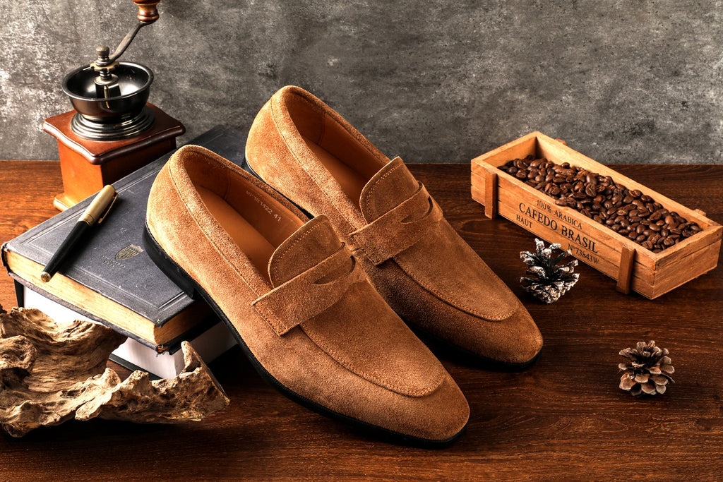Brown loafers on a wooden surface with coffee beans and a coffee grinder.