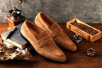 Brown loafers on a wooden surface with coffee beans and a coffee grinder.