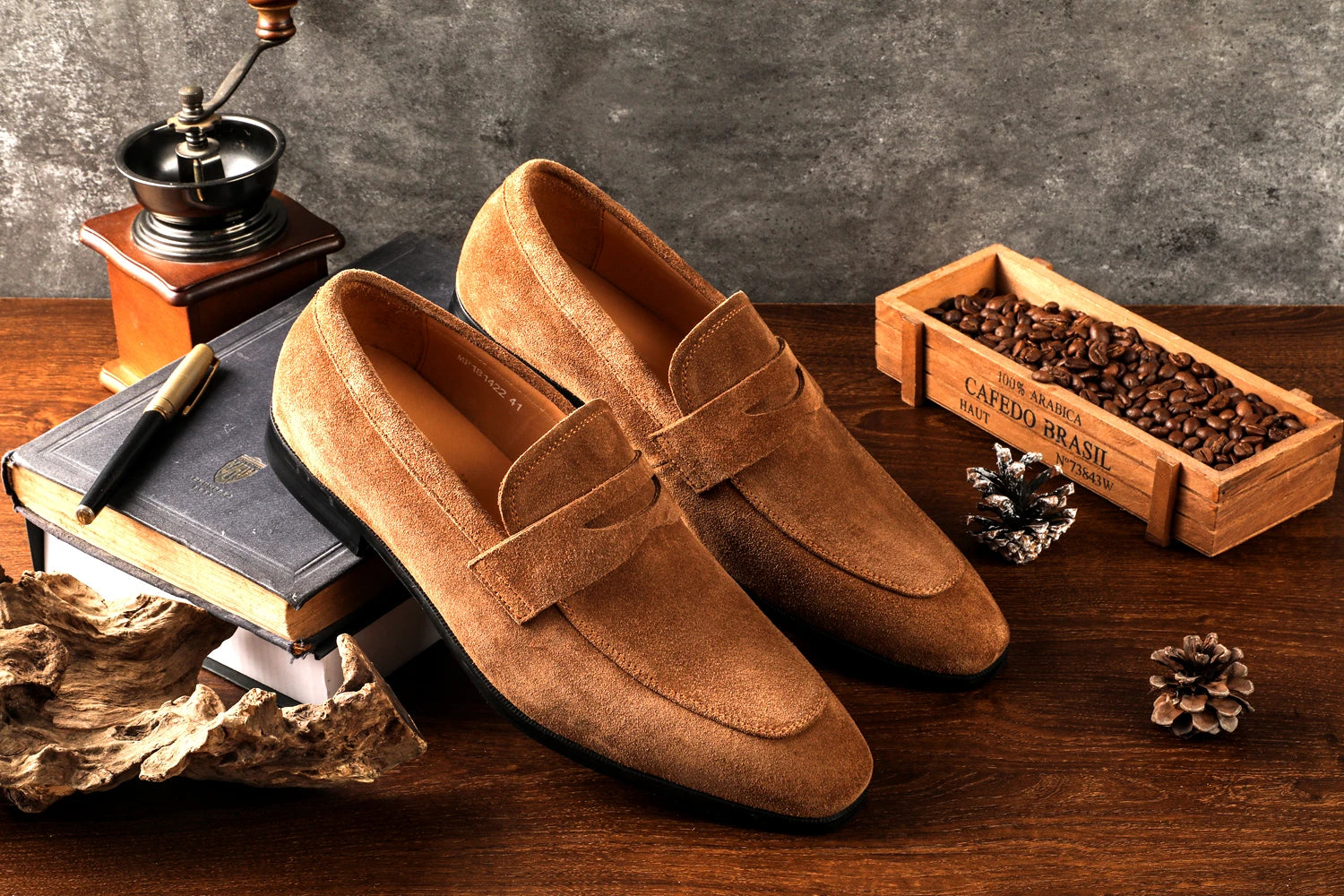 Brown loafers on a wooden surface with coffee beans and a coffee grinder.