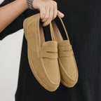 Pair of tan loafers held by a person against a black background