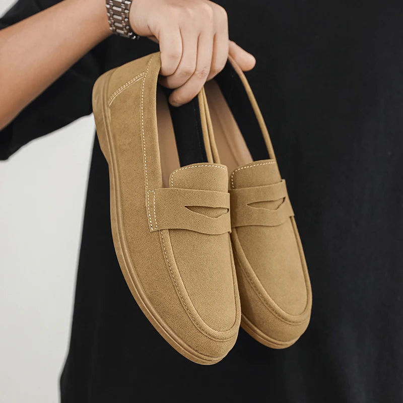 Pair of tan loafers held by a person against a black background