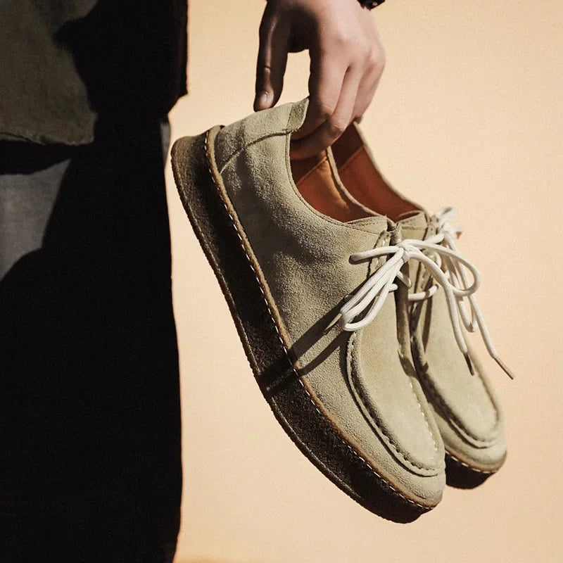 Person holding a pair of green suede shoes with white laces against a beige background