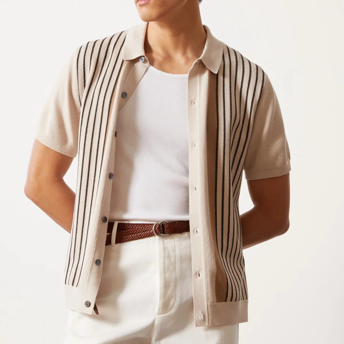 Person wearing a beige shirt with black stripes over a white shirt, on a plain background