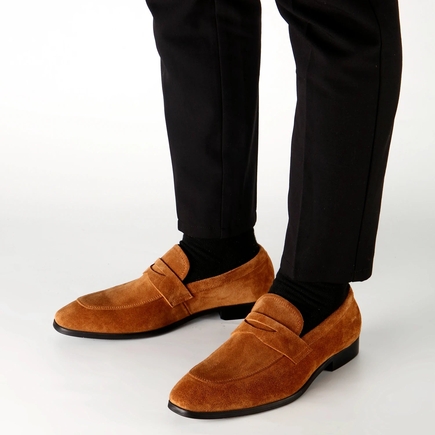 Brown loafers worn with black pants on a white background