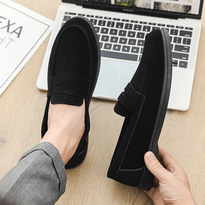 Person wearing black loafers with a laptop on a desk