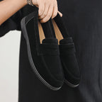 Black loafers held by a person against a black background