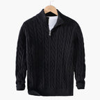 Black cable knit sweater with a zipper on a hanger against a gray background