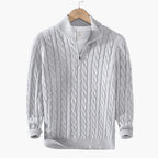 Gray cable knit sweater with a quarter zip on a hanger against a gray background