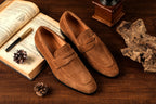 Brown loafers on a wooden surface with an open book and decorative items.
