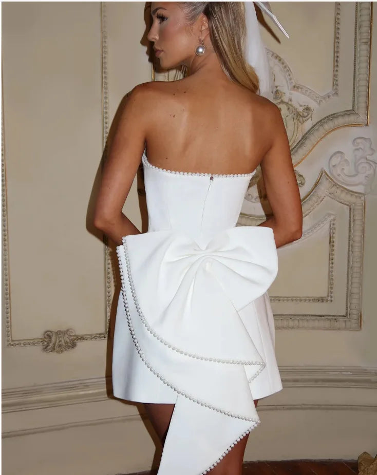 Woman wearing a white strapless dress with a large bow detail in an elegant room.