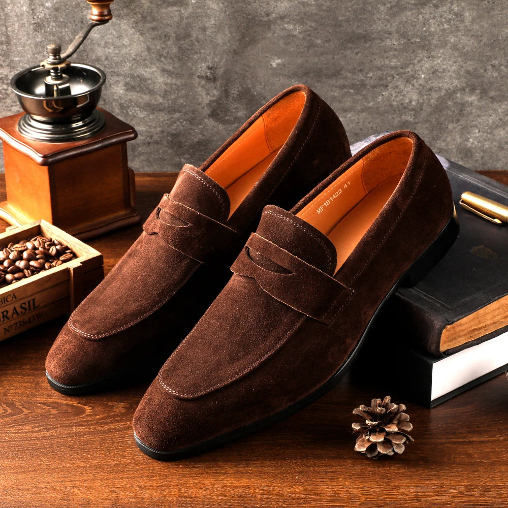 Brown suede loafers on a wooden surface with a coffee grinder and beans in the background.