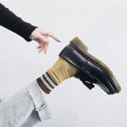 Wearing classic black leather loafers with gray tailored trousers.