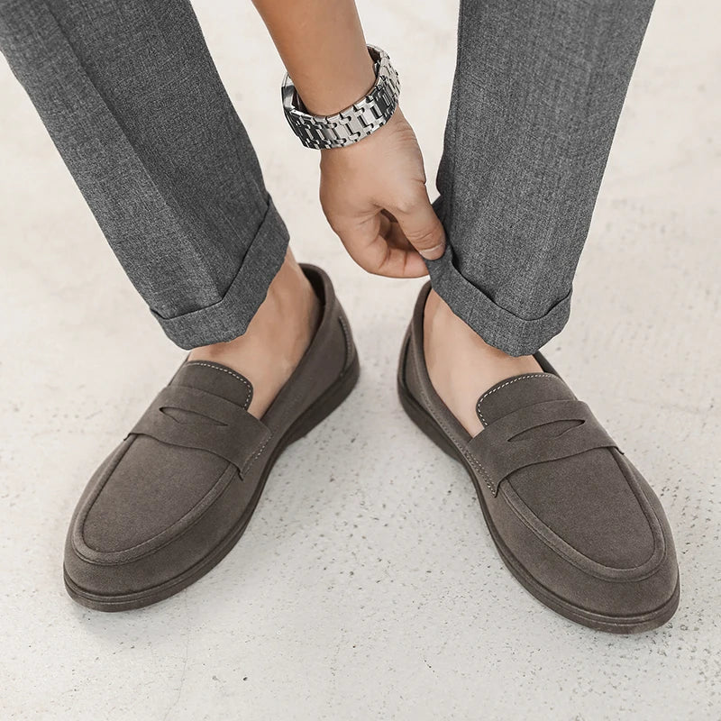 Person wearing gray loafers with rolled-up gray pants on a light background