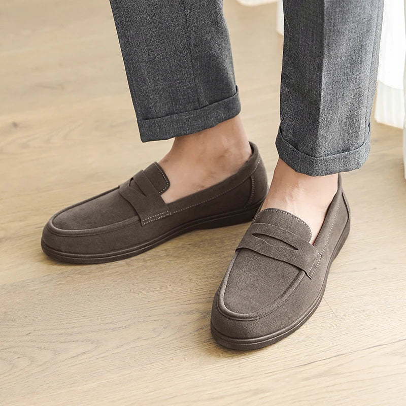 Brown loafers worn with rolled-up gray pants on a wooden floor.