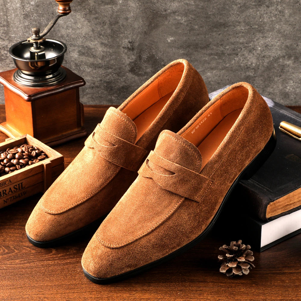 Pair of brown suede loafers on a wooden surface with a coffee grinder and beans in the background.