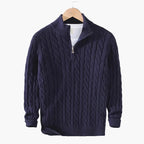 Navy blue cable knit sweater on a hanger against a gray background