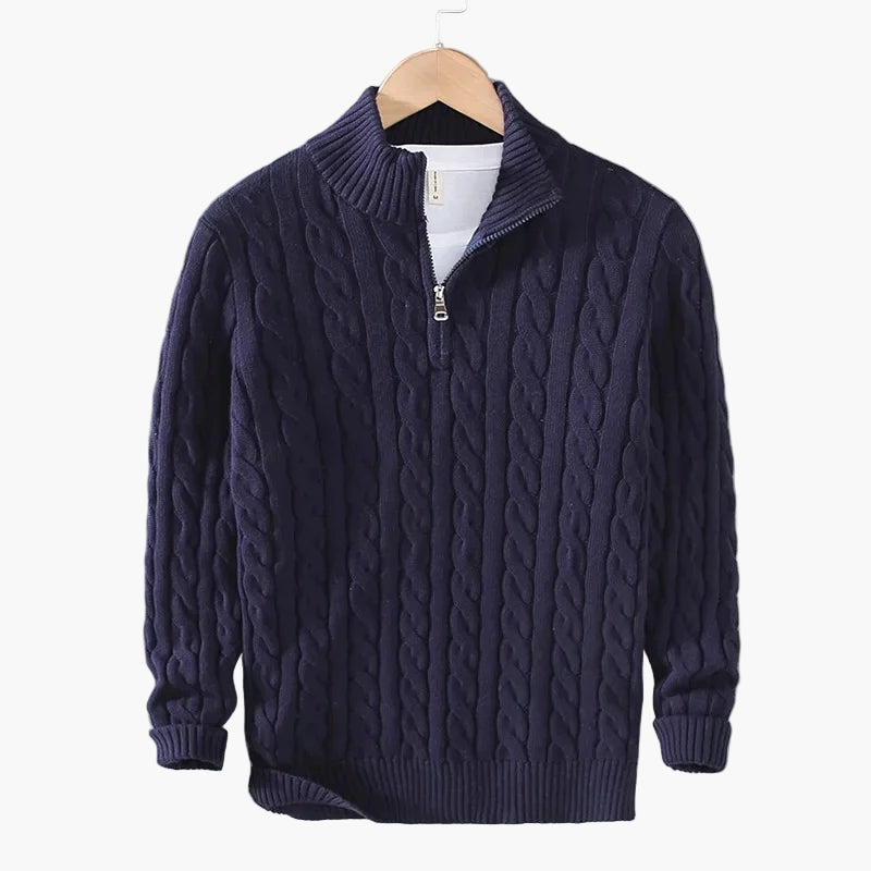 Navy blue cable knit sweater on a hanger against a gray background