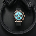 Luxury watch with blue face and black strap on a dark surface with headphones