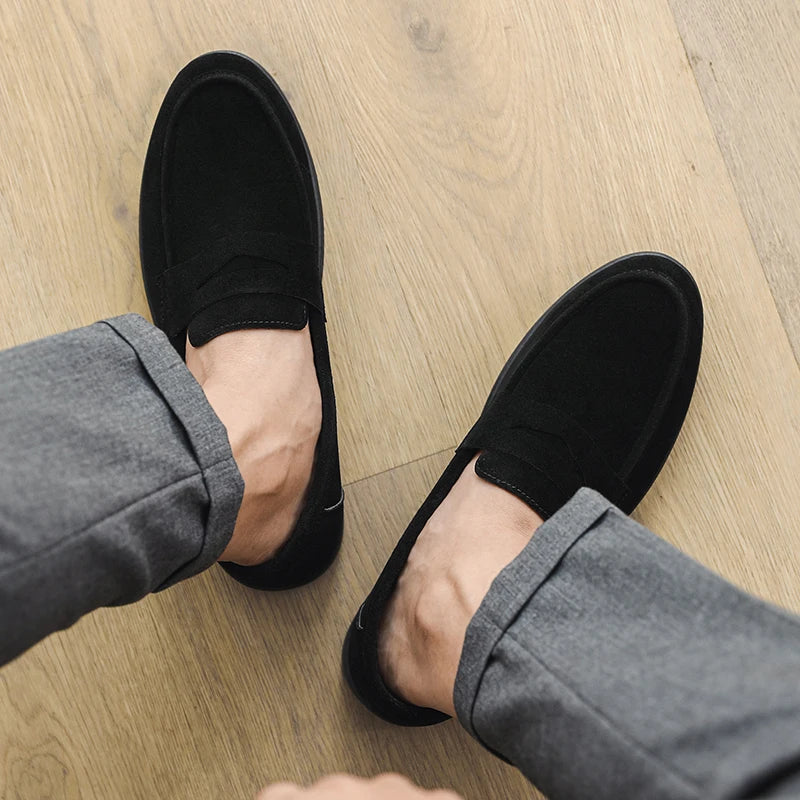 Black loafers worn with gray pants on a wooden floor