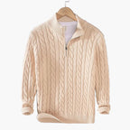 Beige cable knit sweater on a hanger against a gray background