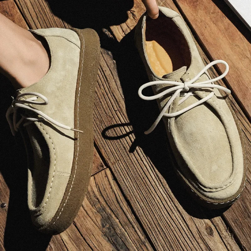 Pair of beige suede shoes with white laces on a wooden surface