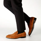 Brown suede loafers worn with black pants on a white background