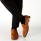 Brown suede loafers worn with black pants on a white background